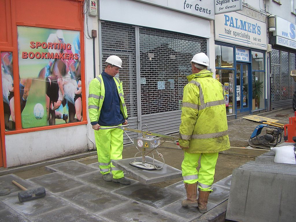 Två arbetare bär med hjälp av vakuumverktyget stenplattor utanför en butik